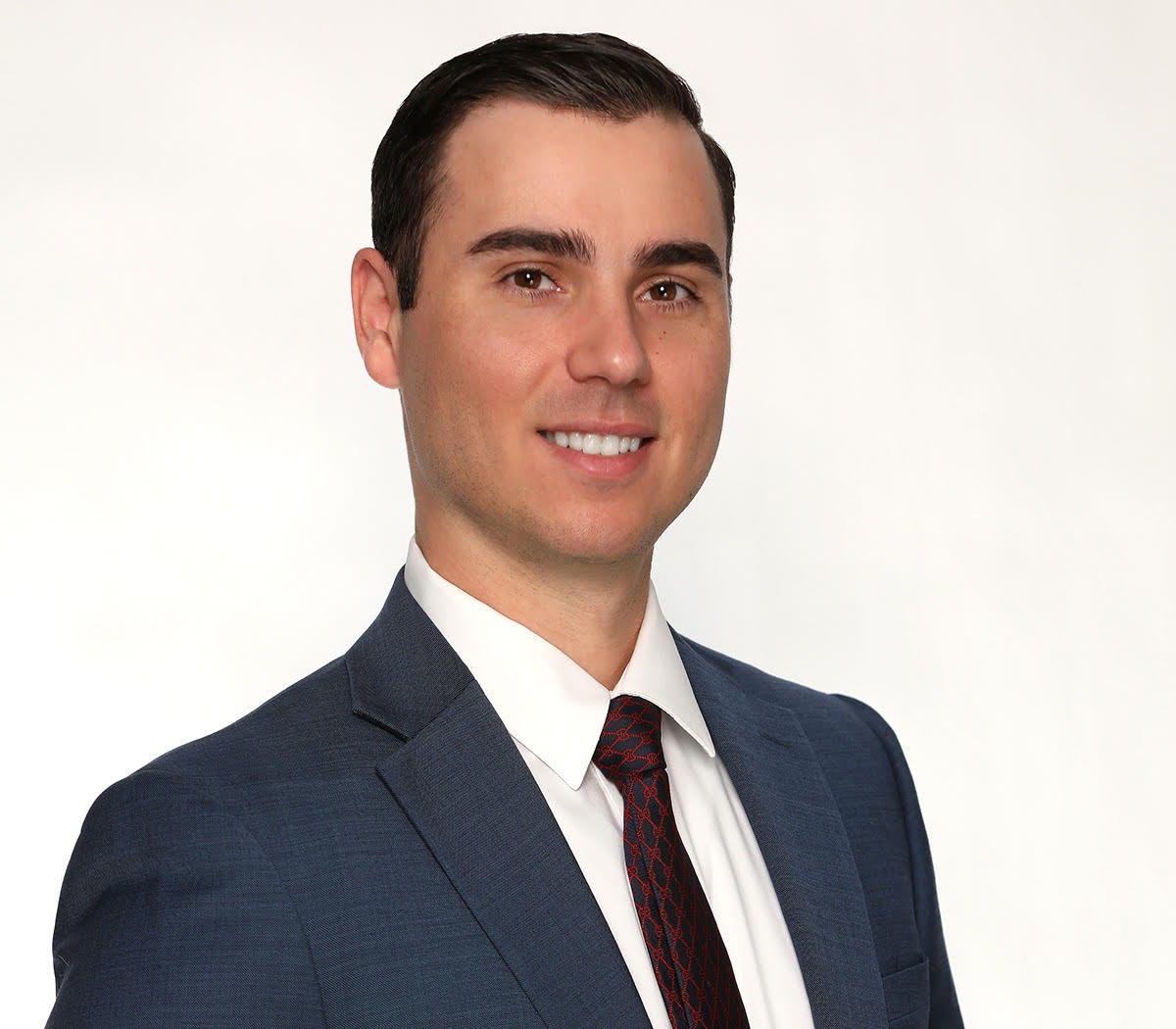 Professional portrait of a man in a navy suit and red tie, smiling at the camera.